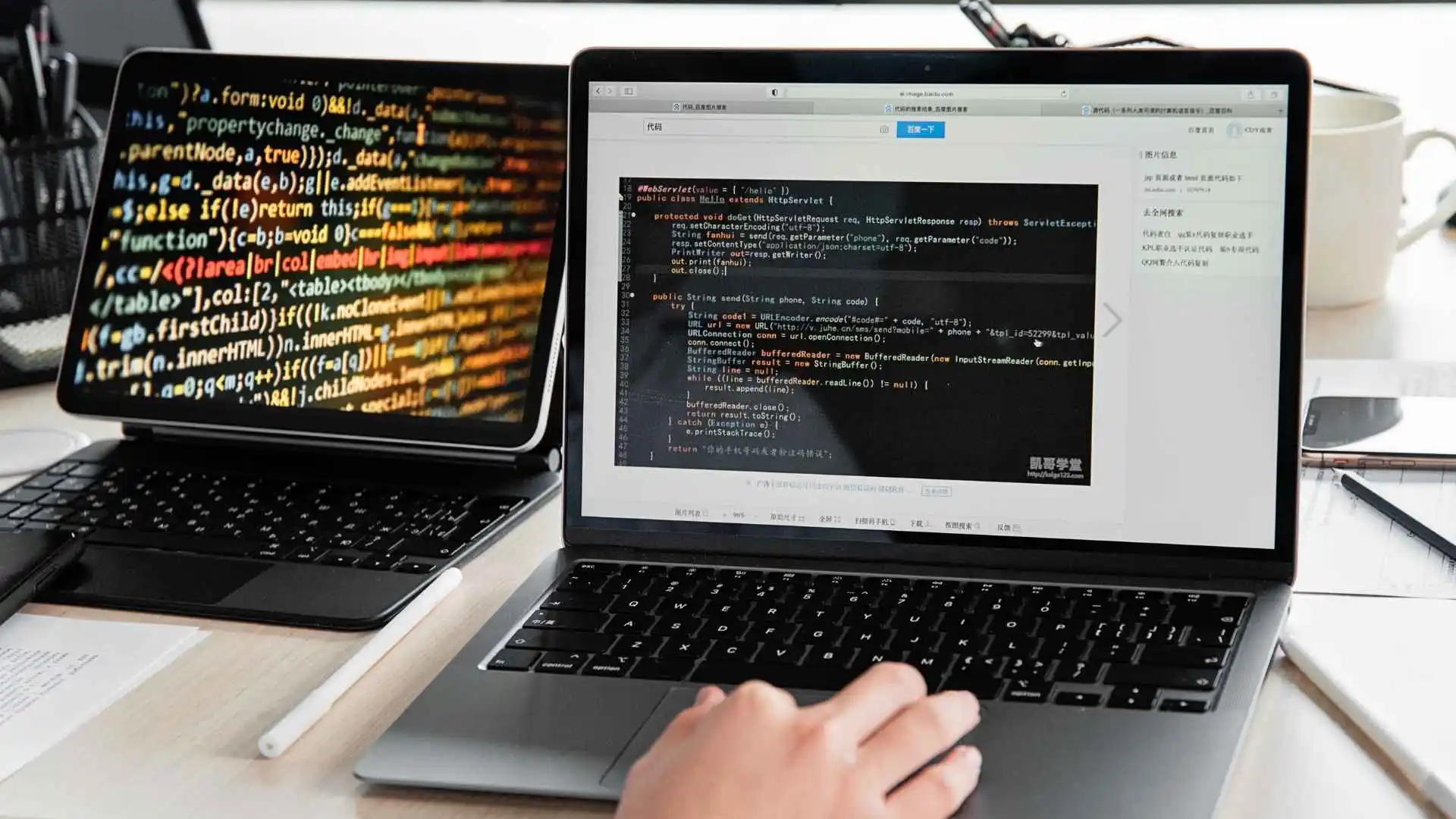 pessoa programando em um notebook com código em Java na tela, ao lado de outro laptop exibindo código colorido em HTML ou JavaScript.
