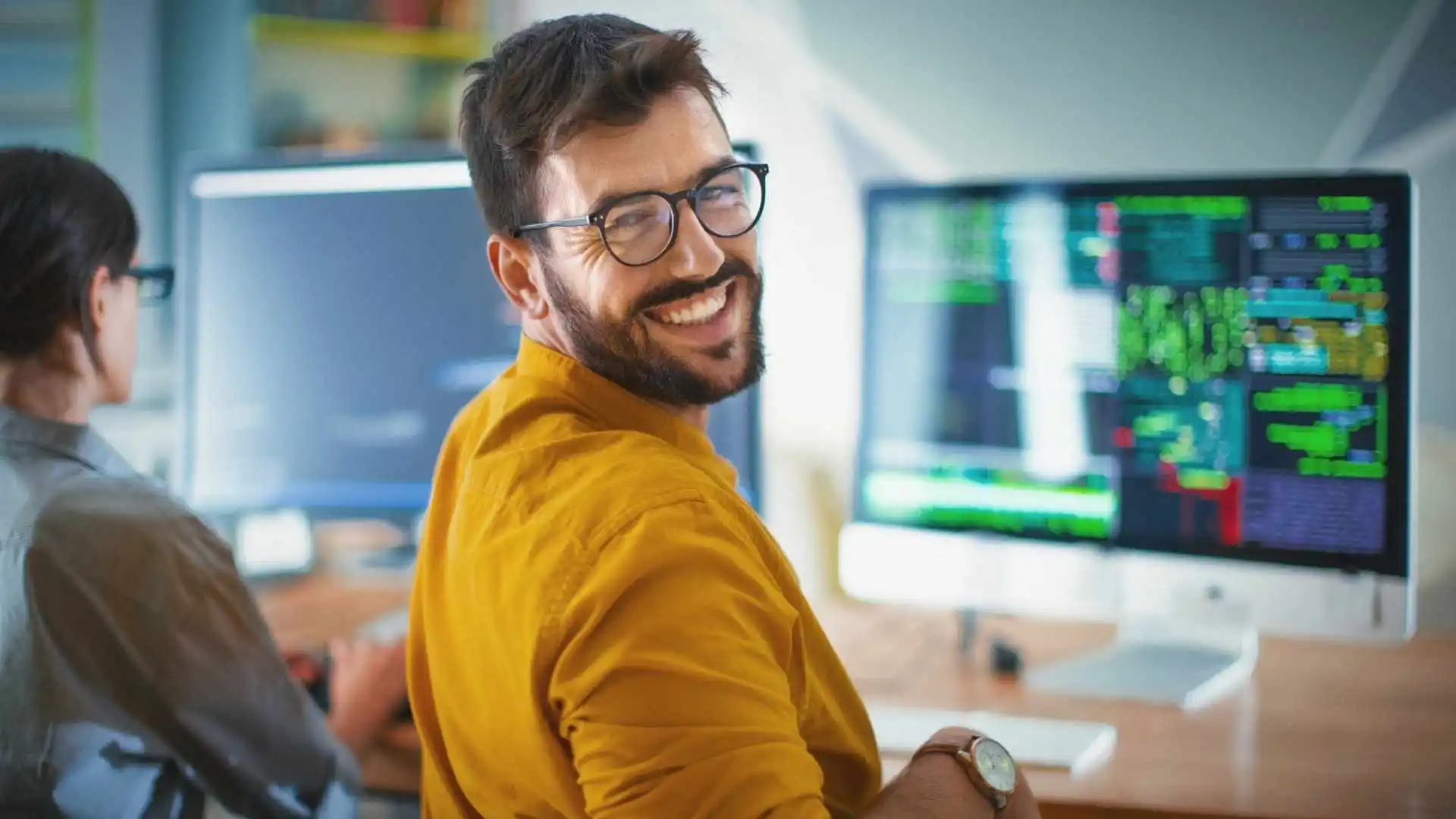 Desenvolvedor backend sorrindo em frente a telas de programação e código no computador