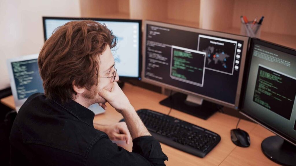 Engenheiro de dados analisando códigos e sistemas em múltiplos monitores durante o desenvolvimento de pipelines de dados