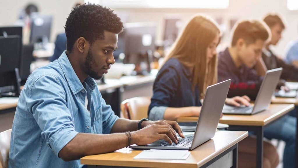 Estudantes participando de um bootcamp de tecnologia, programando em notebooks durante aula prática